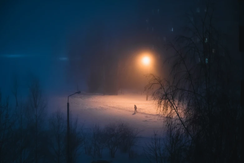 a single person walking across an empty field under a street light