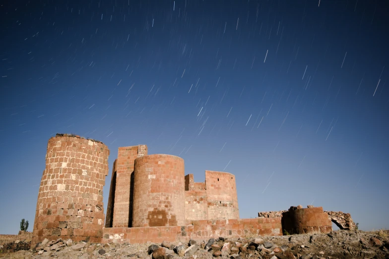 the night sky shines in the background as the ancient stone tower blocks stand tall against a blue sky