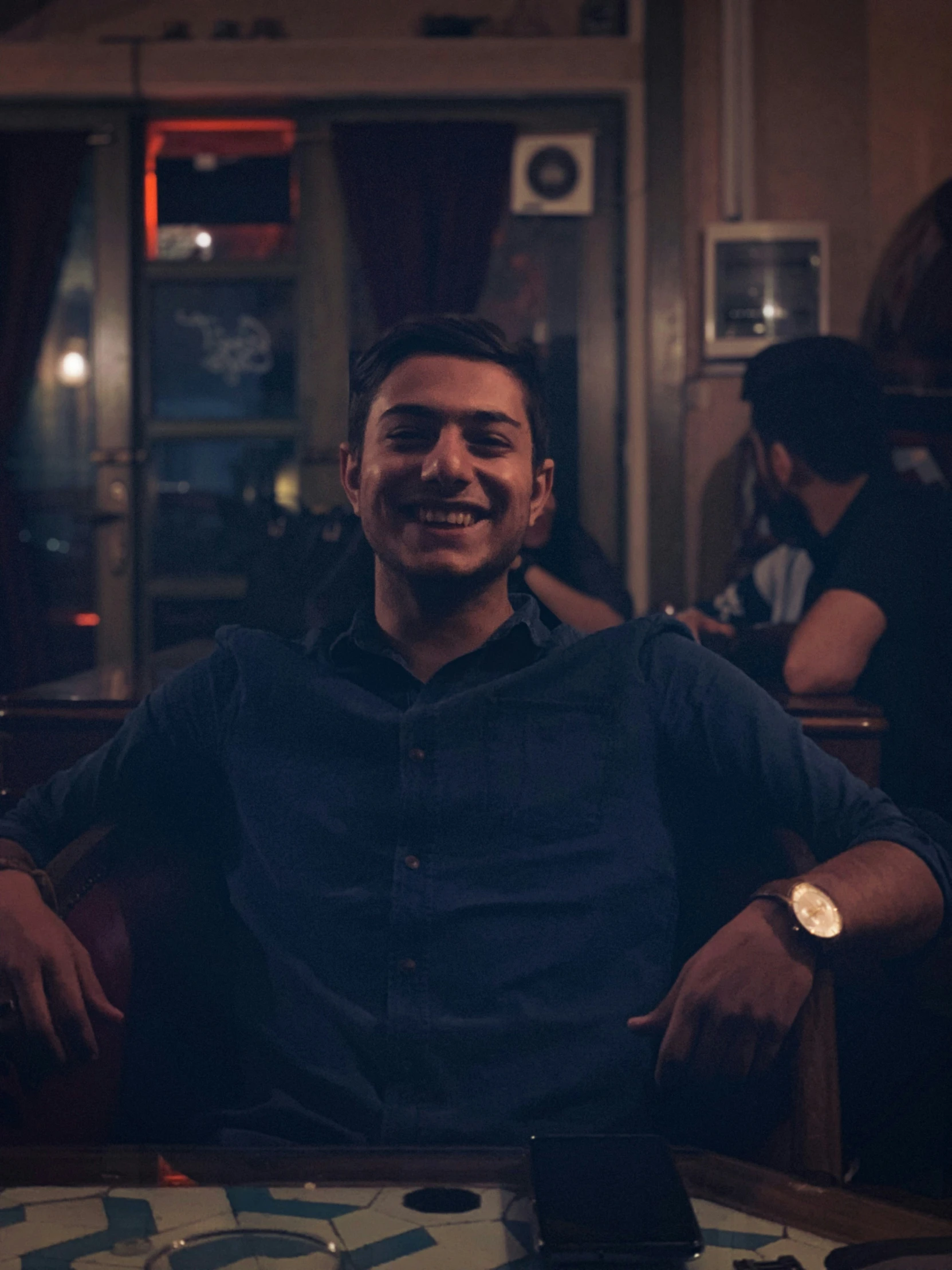 a man smiling in the dark while sitting in a restaurant