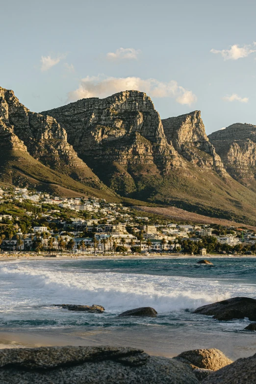 a mountain view with waves in the foreground and houses on a hill in the background