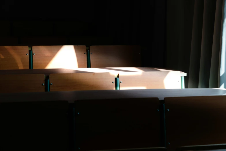 four wooden classroom desks are seen in shadows