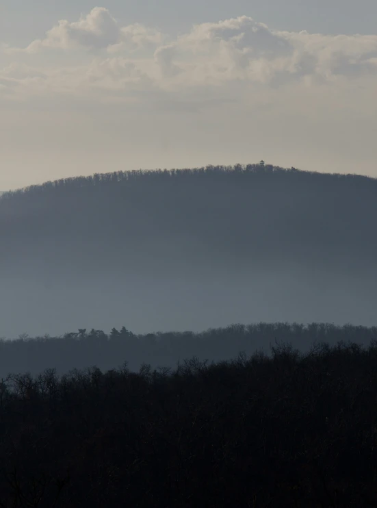 a hilly area with trees silhouetted against the backdrop of a mountain