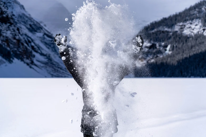 a person standing on their feet splashing with snow in front of mountains