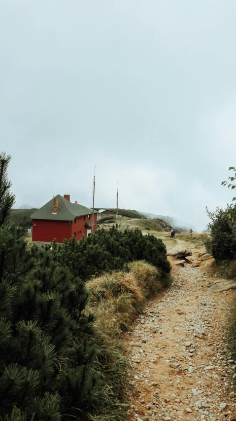 a path leads to an open - sided farm with a red barn and trees