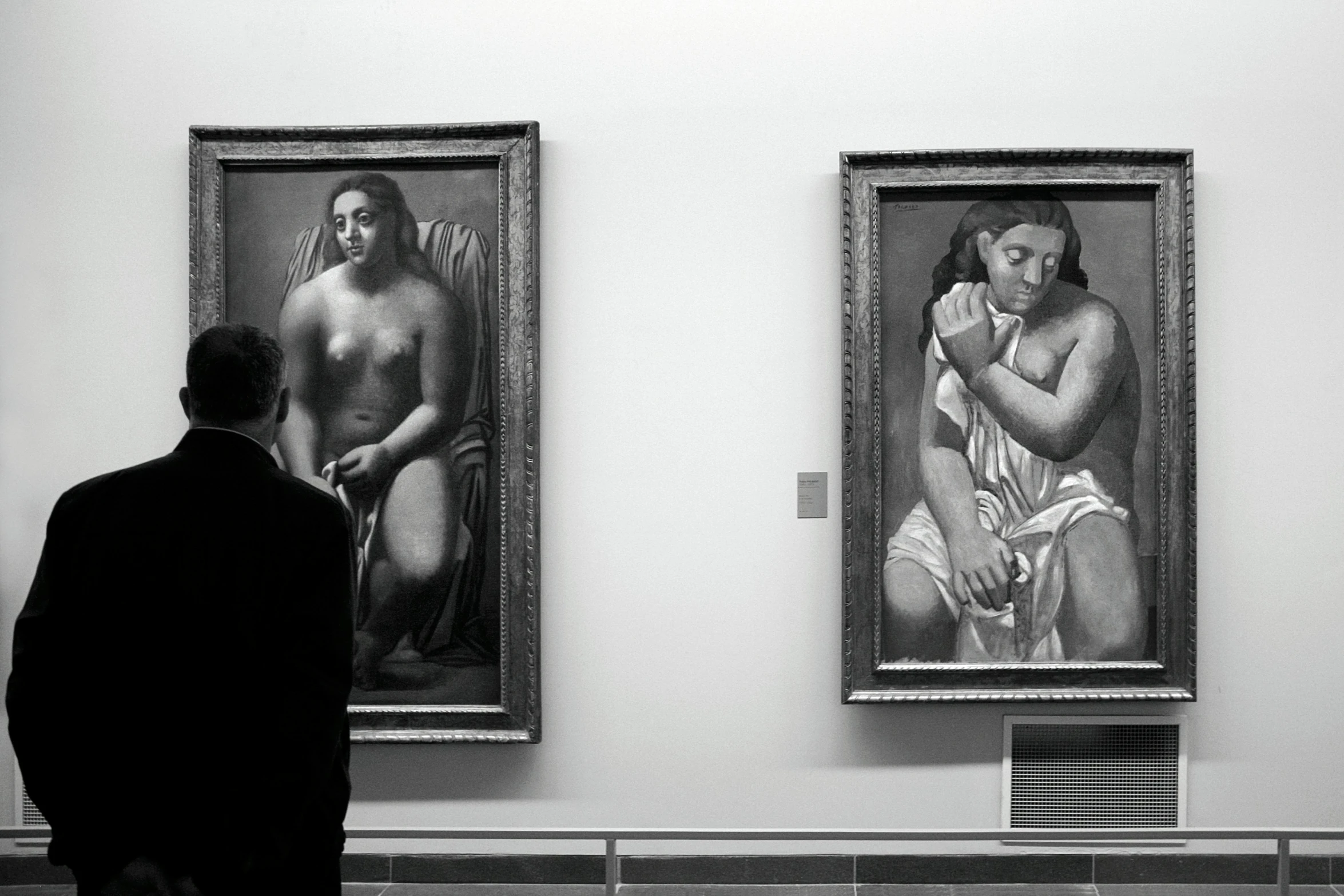 a man looking at two large paintings in a museum