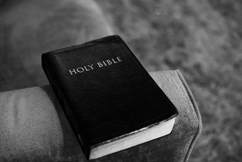 the holy bible is lying on top of the arm of a chair