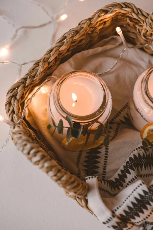 two candles sitting in a woven bag next to a blanket