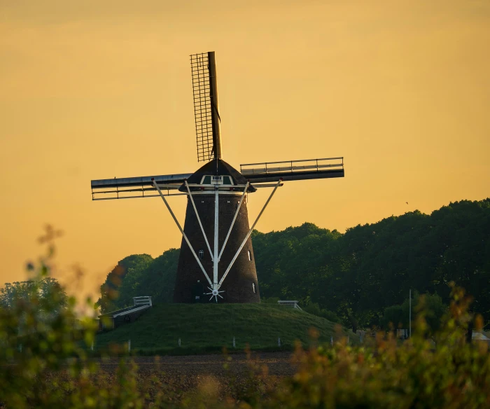 a windmill sits on a hill side surrounded by trees