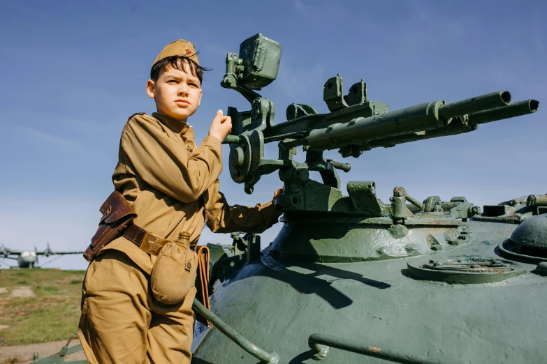 the boy in a uniform stands next to an older style military tank