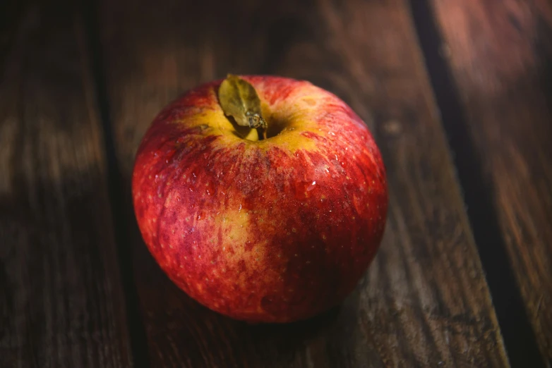 red apple on top of a wooden table with green stem