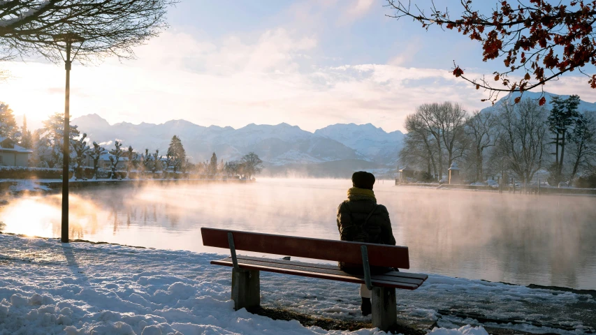 the person sitting on a bench is looking at the water