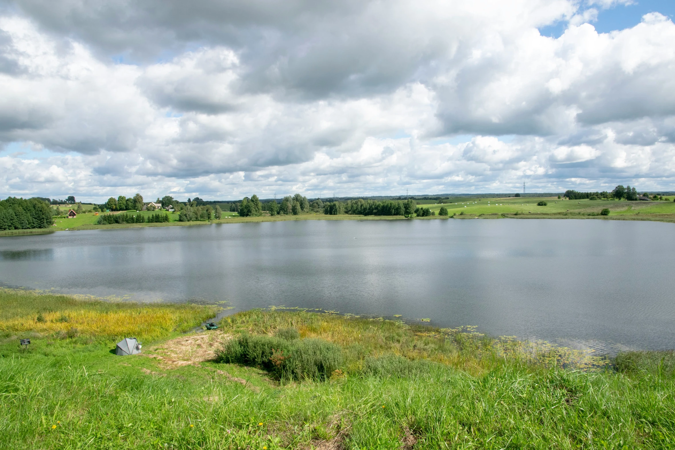 a pond with clouds over it in a grassy field