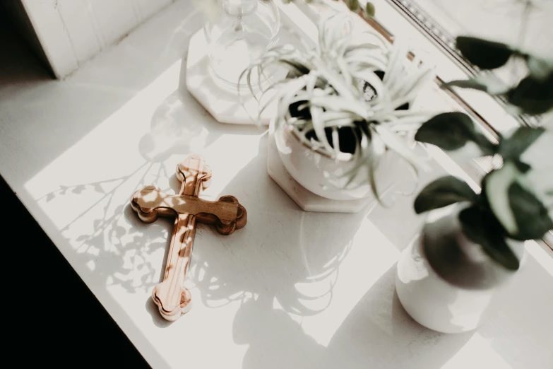 a cross sitting on top of a table near two potted plants