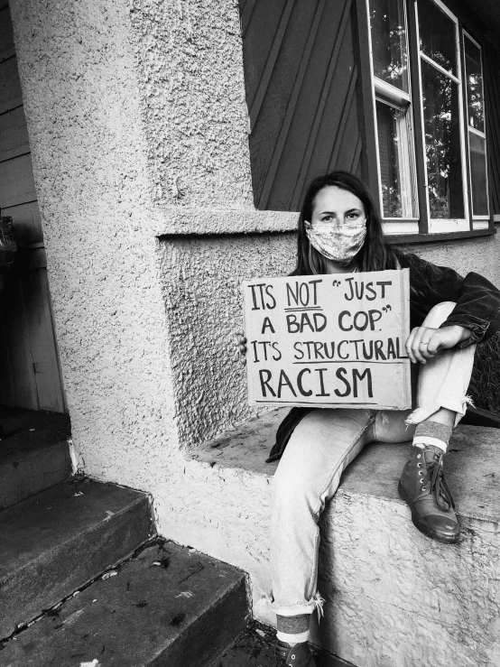 a  with her face mask holding a sign that says, this not just a bad cop it's structural racism