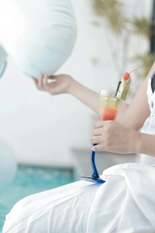 a woman sitting next to the pool holding a glass with an ice drink in it