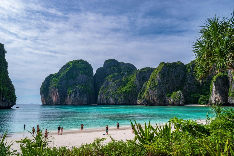 a couple people standing on the beach looking at a rock formation