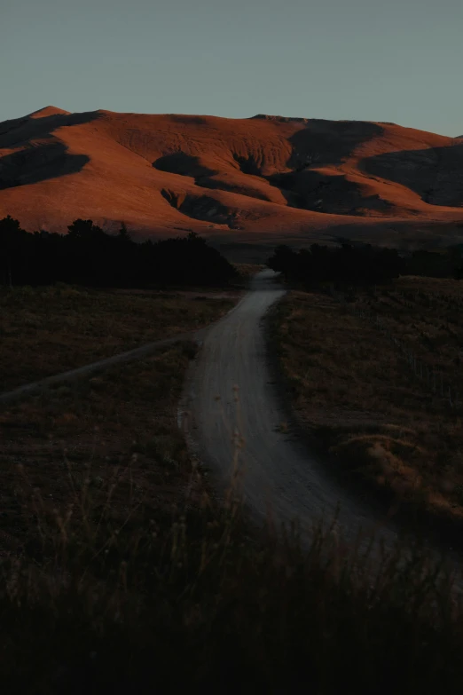 the sun is setting on the hills behind a road