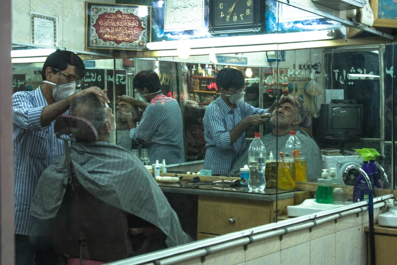 a barber shaves the client's hair as the shopkeeper looks on