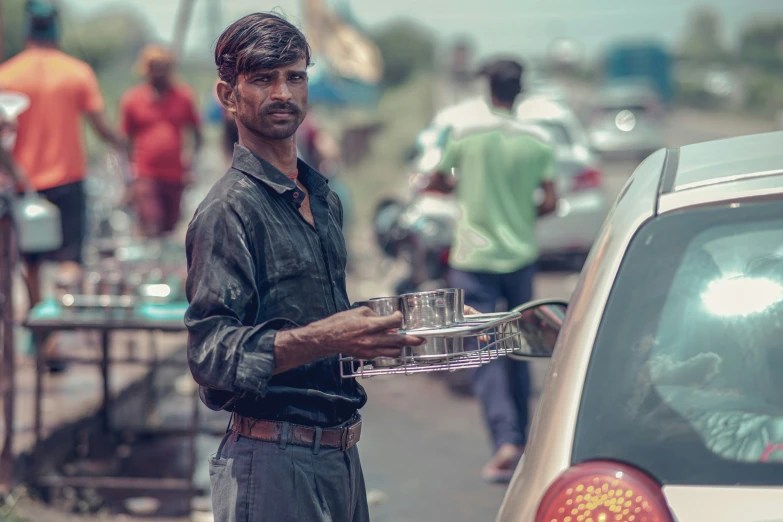 a man stands in front of a car and holds a cup