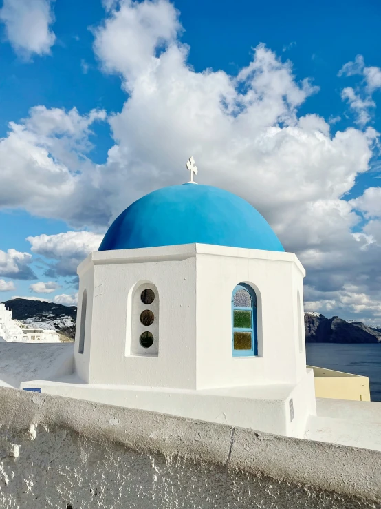 a small blue dome near the ocean under a blue and white cloudy sky