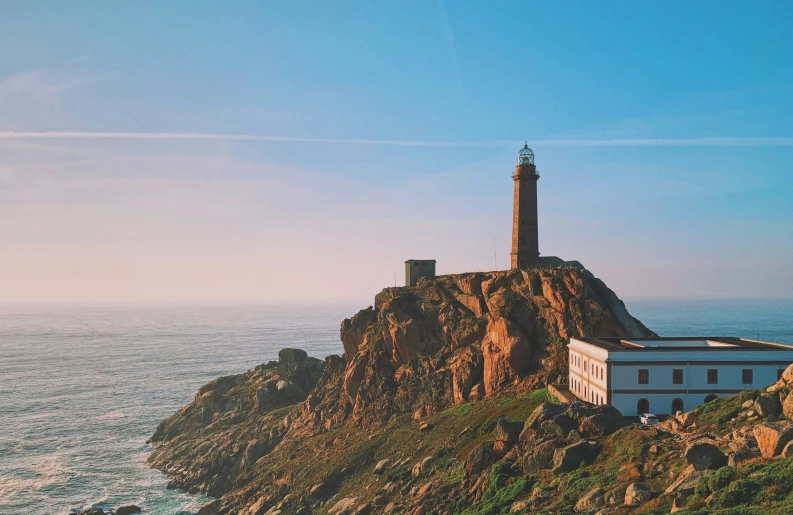 a long lighthouse on top of a cliff next to the ocean