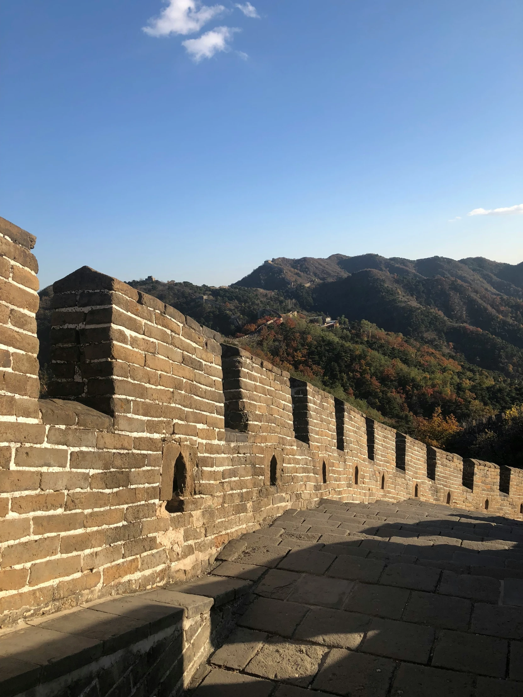 a very tall and narrow brick wall with a steep mountain in the background