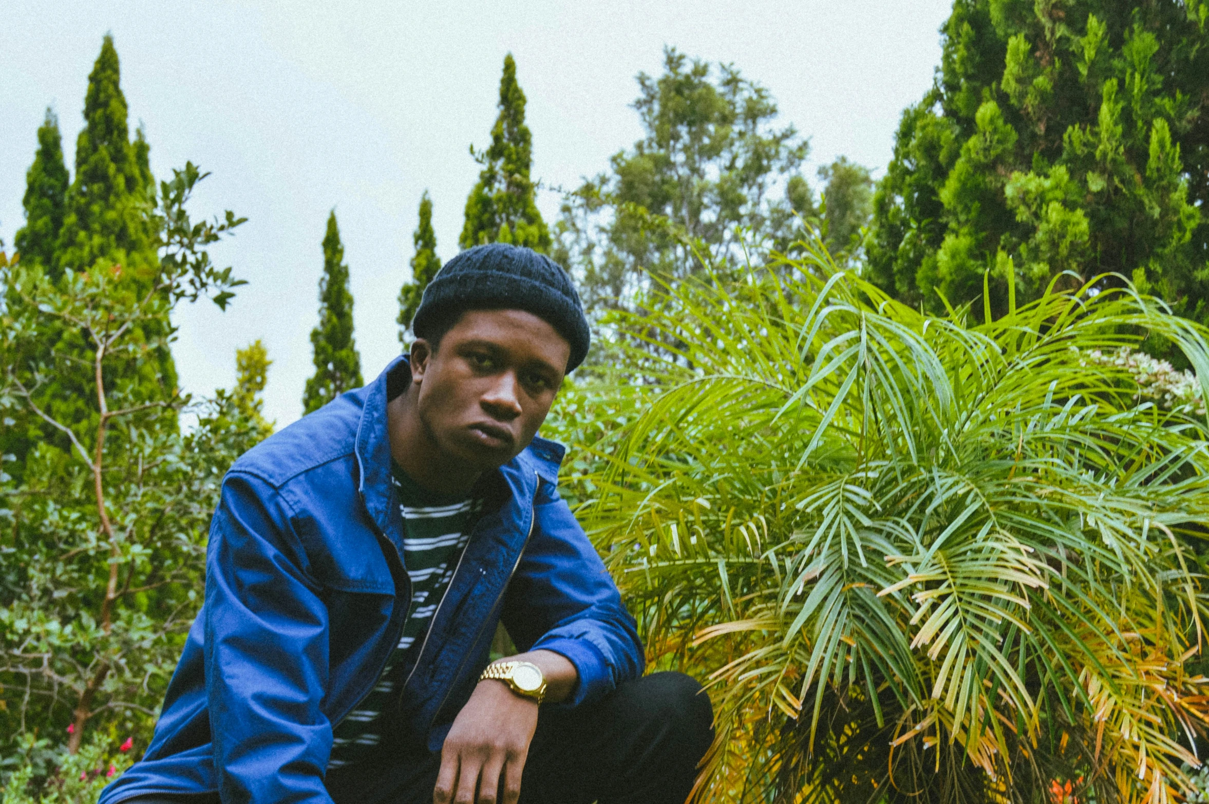 a man squatting and standing outside by plants