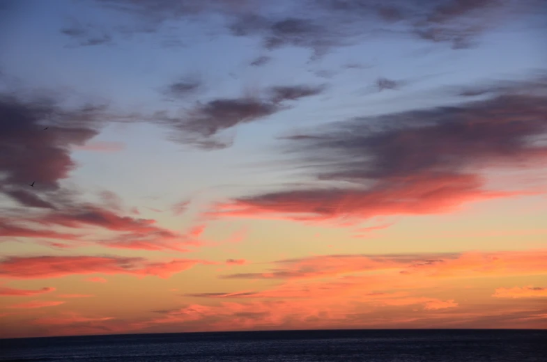 some clouds are seen in the sunset with an airplane in the distance