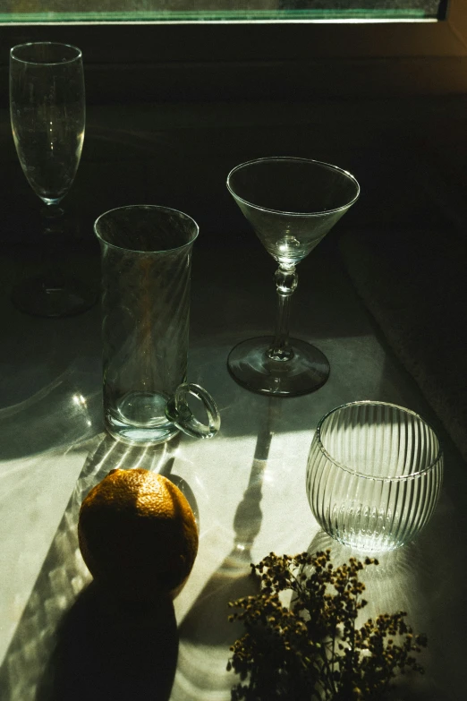 three glasses and an orange sit on a windowsill