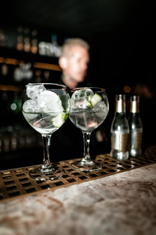 two wine glasses sit on a bar next to the bottles