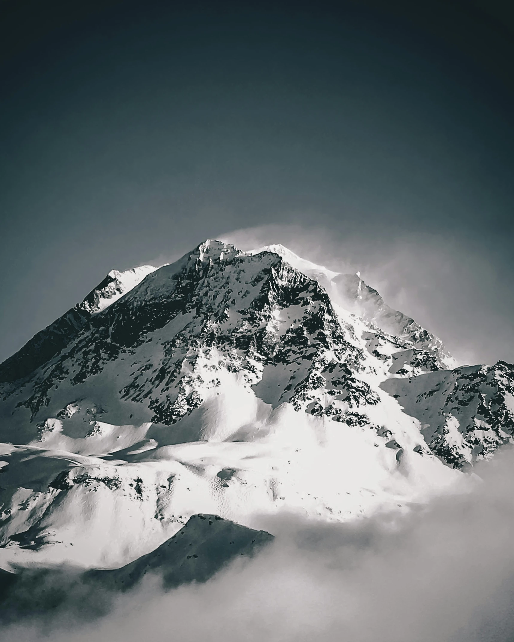 a big mountain surrounded by clouds in the day