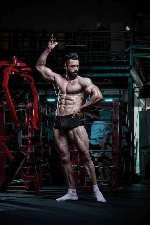 shirtless male muscle bodybuyer posing in front of red apparatus