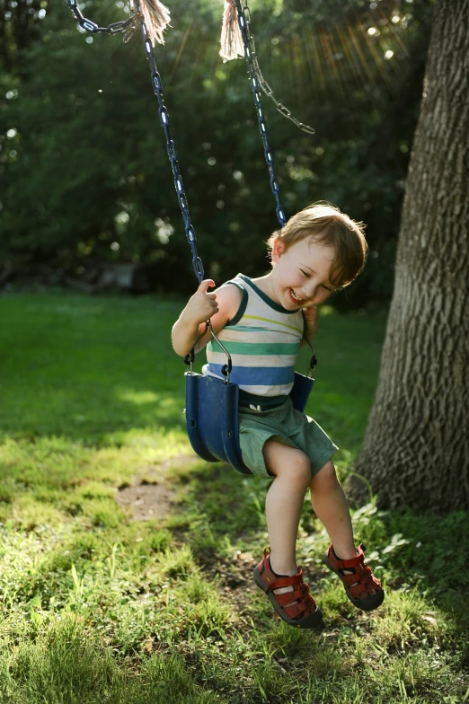 a little boy sitting on a swing in a grassy park