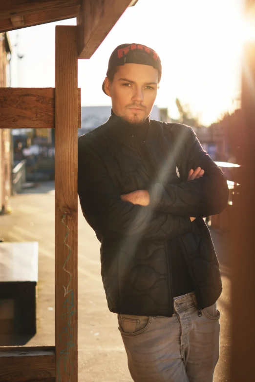 man in denim jacket and hat leaning on wooden structure