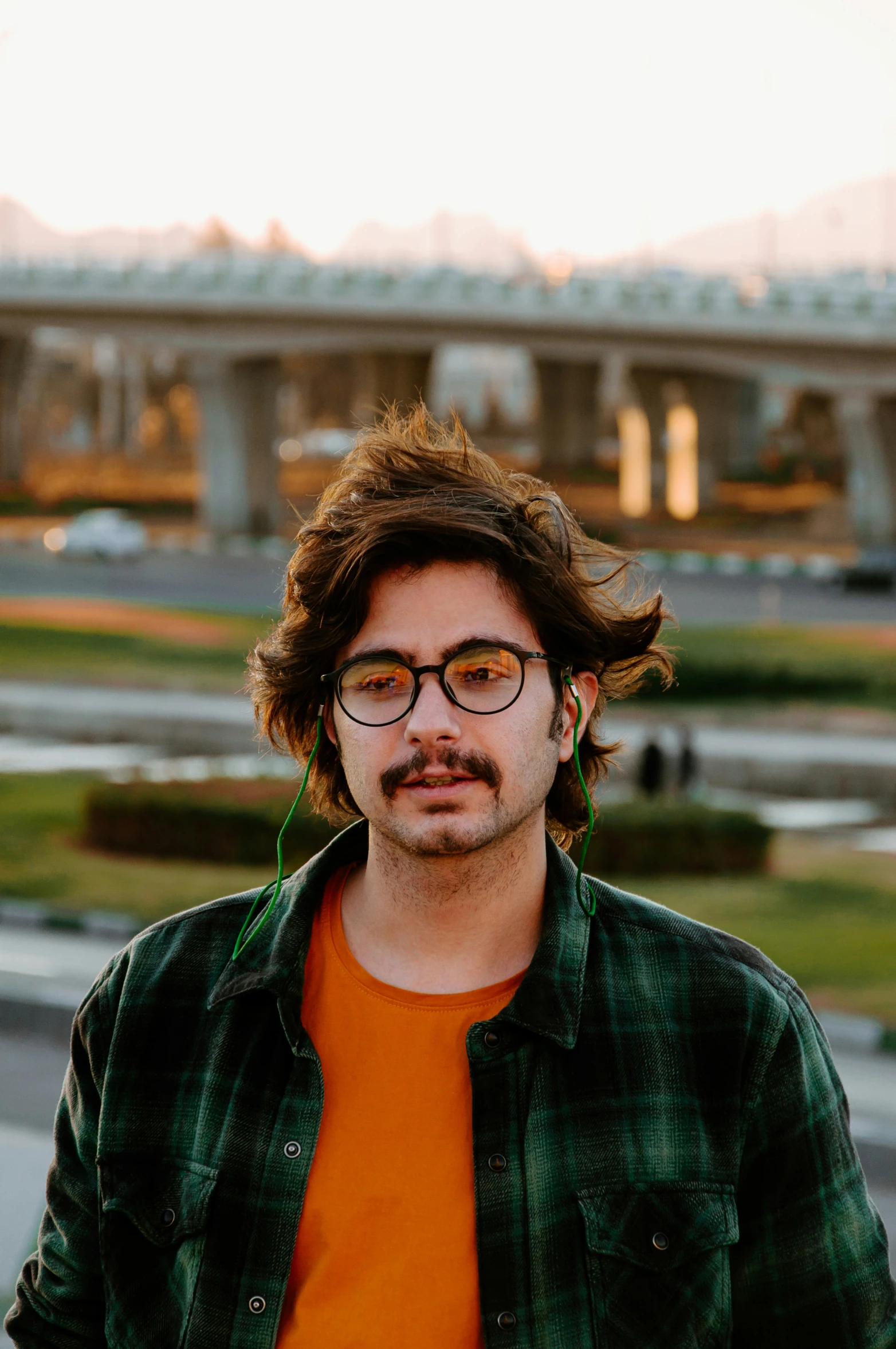 a man with long hair and glasses stands on the side walk