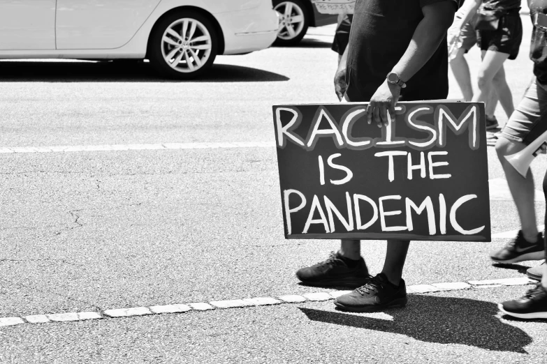 a protest sign that reads racism is the pandemic