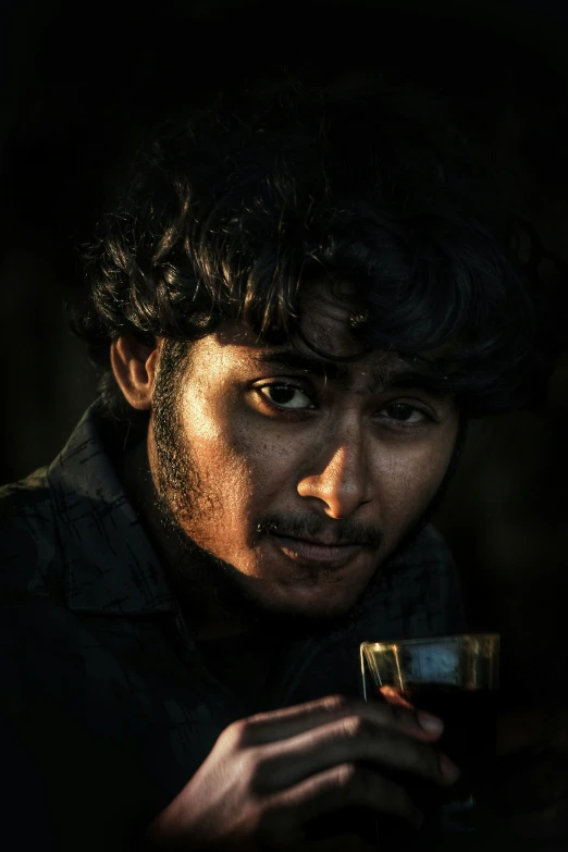 a man stares into the camera as he holds a cup in his hand