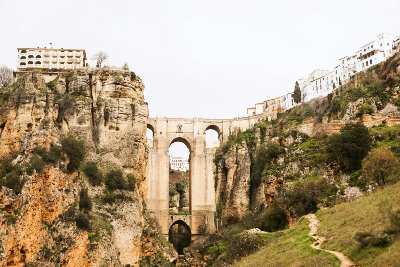 a stone bridge going over a steep gorge under a cloudy sky