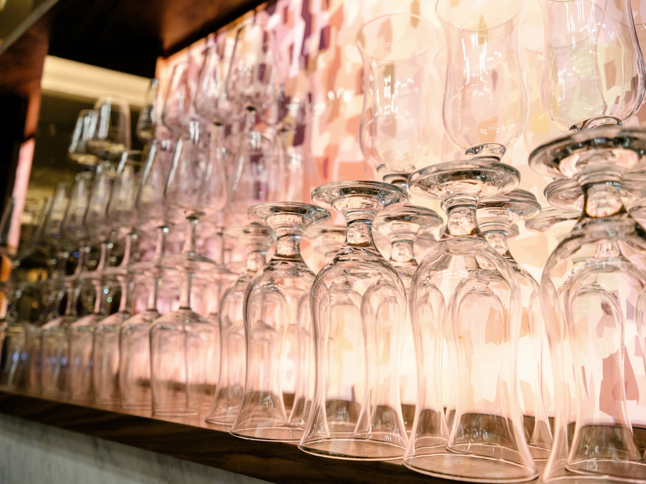 rows of empty wine glasses sit in rows, next to a line of other glasses