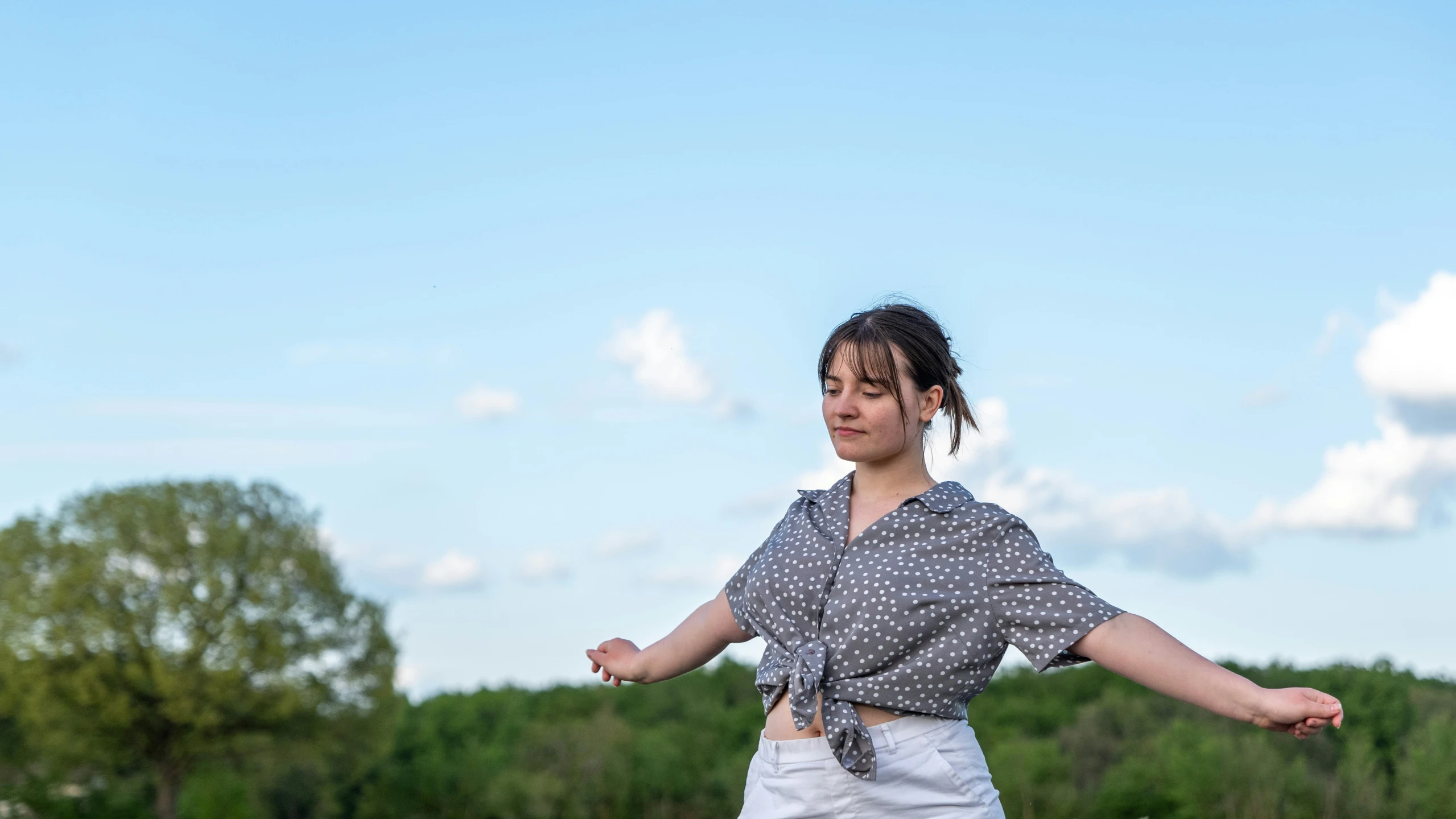 a woman wearing a polka dot blouse standing in a field