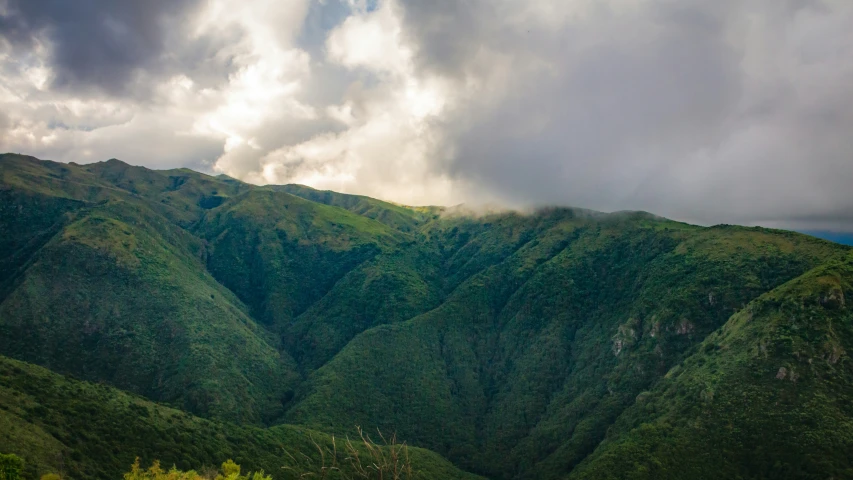 a large green mountainside with clouds in the distance