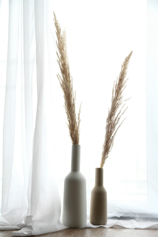 two vases sitting on top of a floor next to a curtain