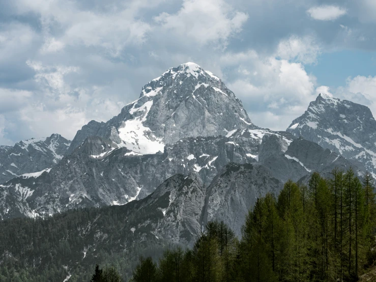 a view of the top of a mountain, with trees in the foreground and clouds overhead