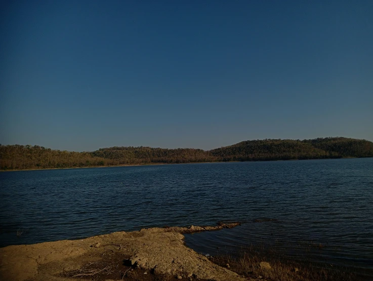 a person is sitting on a beach in front of a large lake