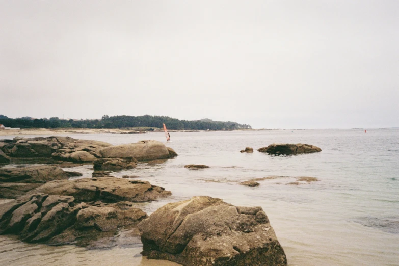 a man stands at the water's edge near some rocks