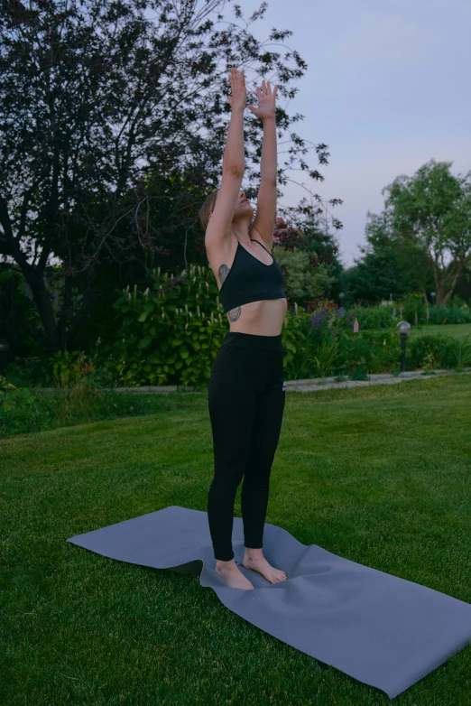 a woman practices yoga on a yoga mat in the backyard