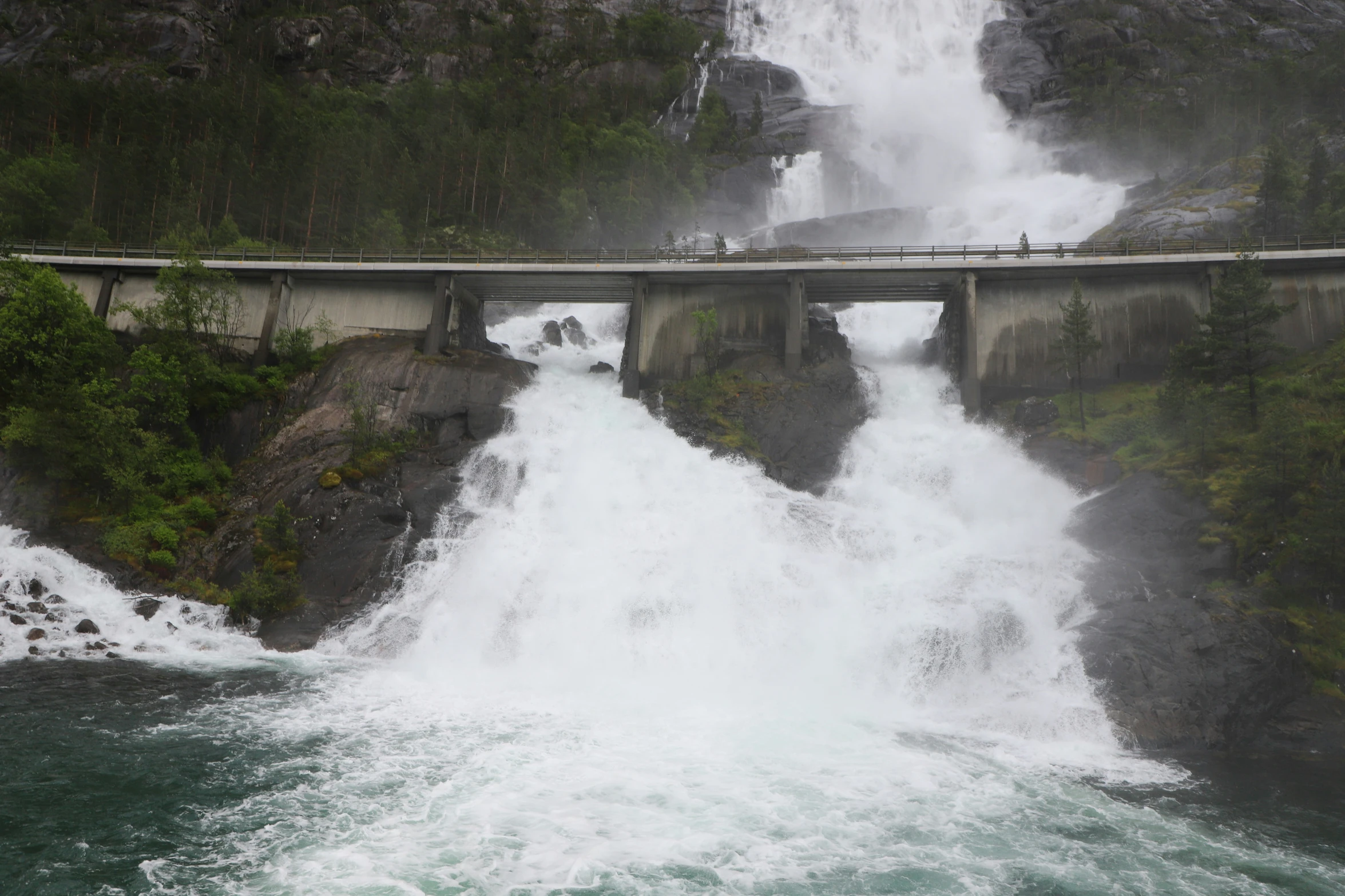 two people stand on the bridge overlooking the water that flows into the falls