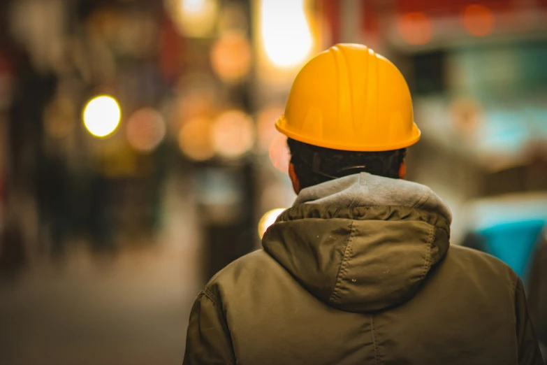 man in yellow hard hat looking across a busy street