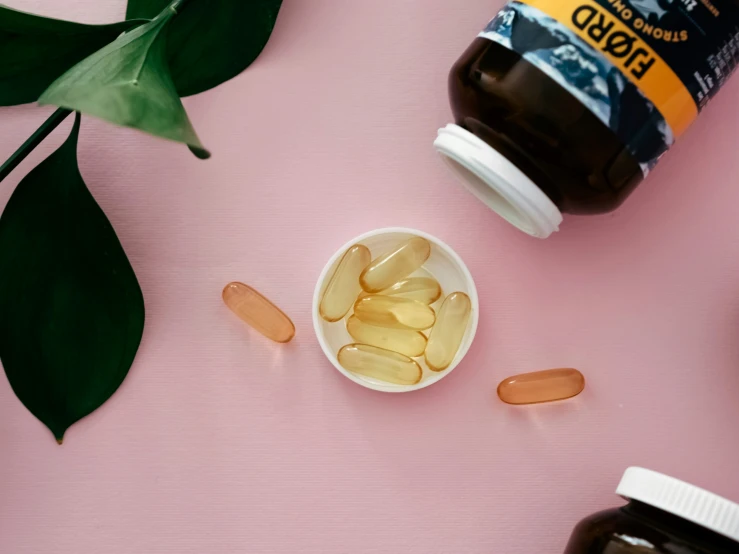 two different pills on a pink surface with bottles nearby