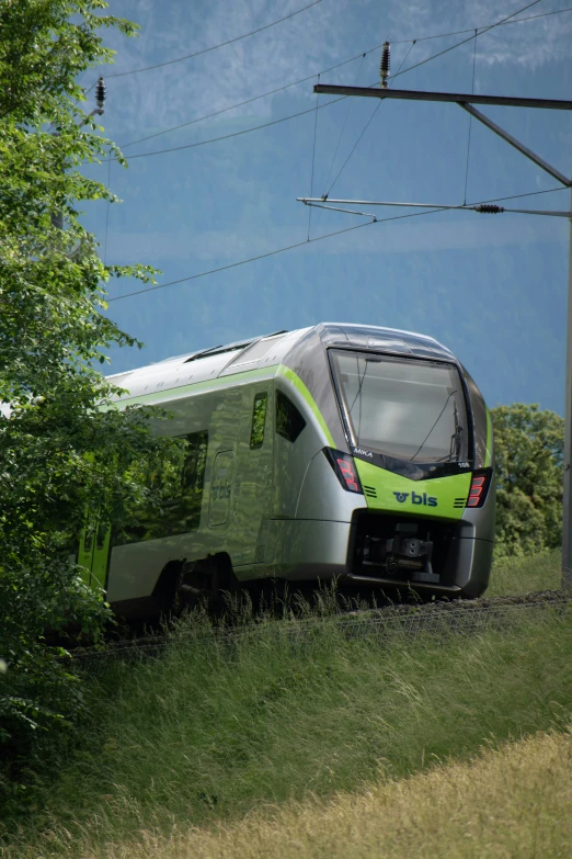 the green train is traveling down the tracks by some trees